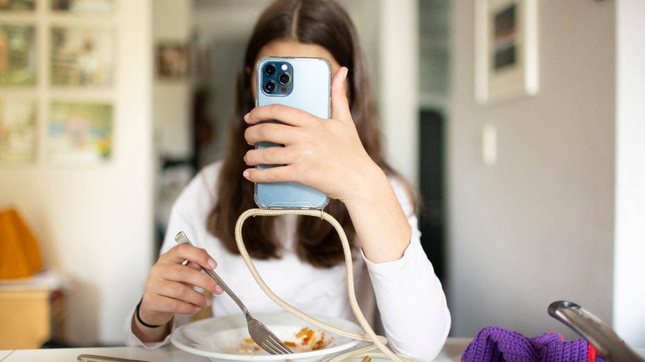 In this photo illustration a young girl is sits behind her plate with food and is playing with her smartphone on May 03, 2021 in Bonn, Germany. (Photo by Ute Grabowsky/Photothek via Getty Images)