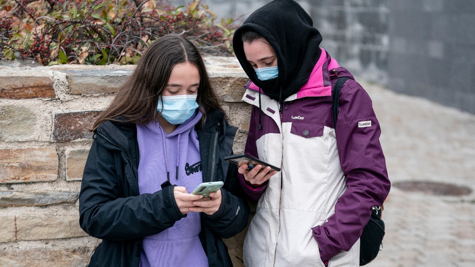 Two girls with face masks looking at their mobile phones, the day before the entry into force of the mandatory use of masks outdoors, on December 23, 2021 in Madrid, Spain.  (Photo by Eduardo Parra/Europa Press via Getty Images)