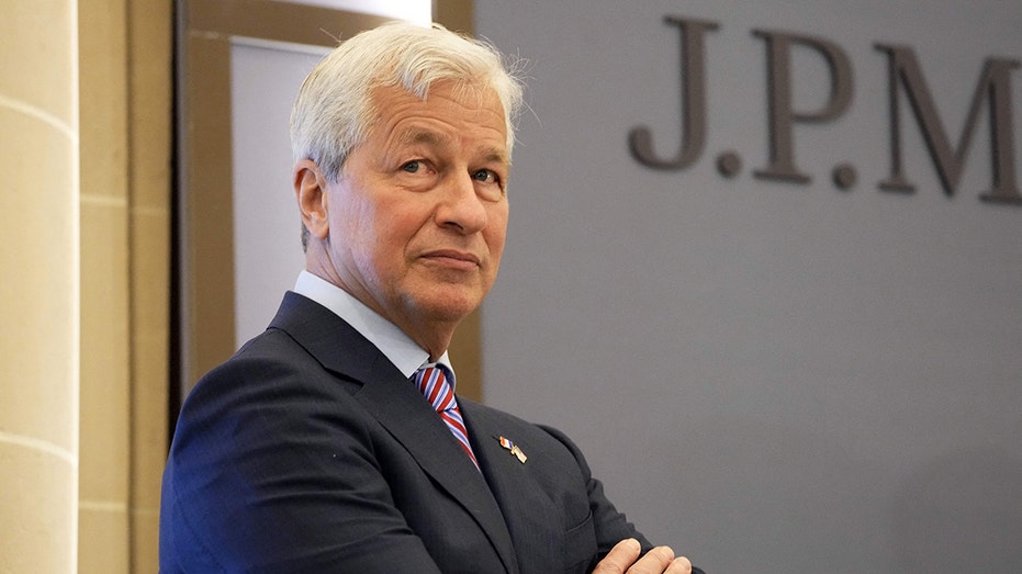 Jamie Dimon JP Morgan standing behind a JP Morgan logo