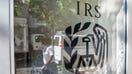 The reflection of a pedestrian is seen walking past an Internal Revenue Service (IRS) office building in the East Harlem neighborhood of New York, U.S., on Saturday, June 24, 2017. The IRS online registration system for social welfare organizations will be updated to streamline the payment process, by combining the application and payment fee. Photographer: Timothy Fadek/Bloomberg via Getty Images