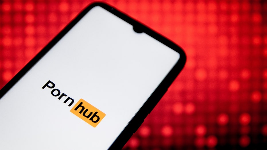 A PornHub logo seen displayed on a smartphone screen with a computer wallpaper in the background
