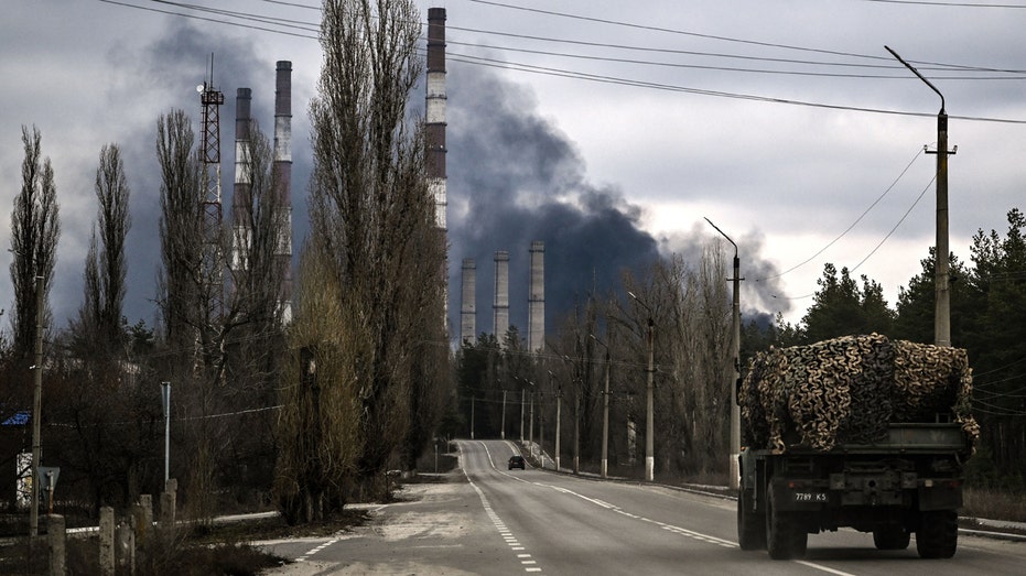 A military vehicle drives on a road as smoke rises from a power plant after shelling outside the town of Schastia, near the eastern Ukraine city of Lugansk, on Feb. 22, 2022, a day after Russia recognized east Ukraine's separatist republics and ordered the Russian army to send troops there as "peacekeepers." 