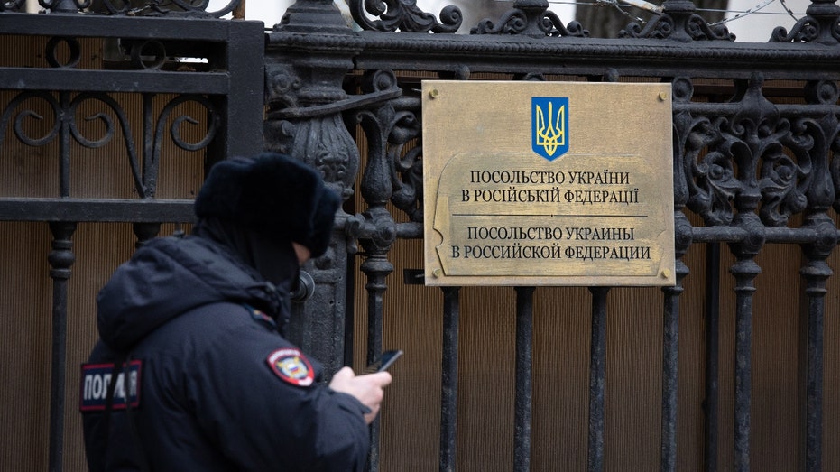 A police officer checks his smartphone during a patrol at an entry gate at the Embassy of Ukraine building in Moscow, Russia, on Thursday, Feb. 24, 2022. Photographer: Andrey Rudakov/Bloomberg