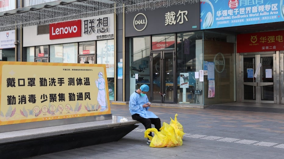A janitor checks his phone outside closed shops in Huaqiangbei area