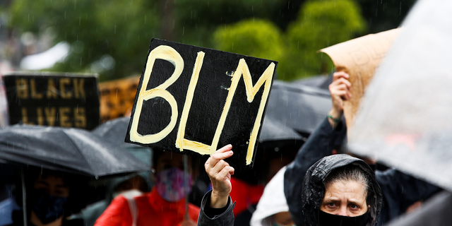 A woman is holding a "BLM" sign in the rain during a silent march organized by Black Lives Matter in Seattle, Washington on June 12, 2020 to protest racial inequality following the death of George Floyd.