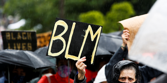 A woman holds a "BLM" sign in the rain as tens of thousands of people participate in a silent protest march organized by Black Lives Matter Seattle-King County as people protest against racial inequality in the aftermath of the death in Minneapolis police custody of George Floyd in Seattle, Washington, U.S. June 12, 2020. REUTERS/Lindsey Wasson