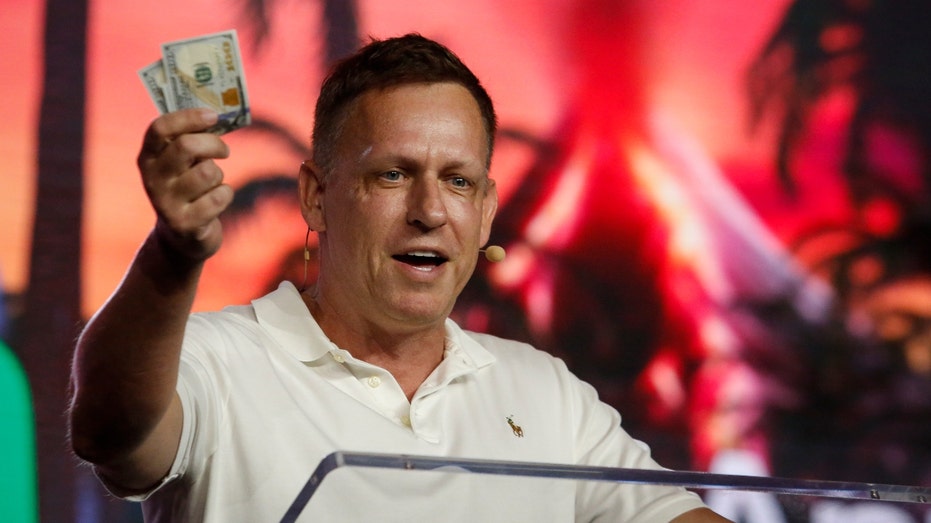 Peter Thiel, co-founder of PayPal, Palantir Technologies, and Founders Fund, holds hundred dollar bills as he speaks during the Bitcoin 2022 Conference at Miami Beach Convention Center on April 7, 2022 in Miami, Florida.