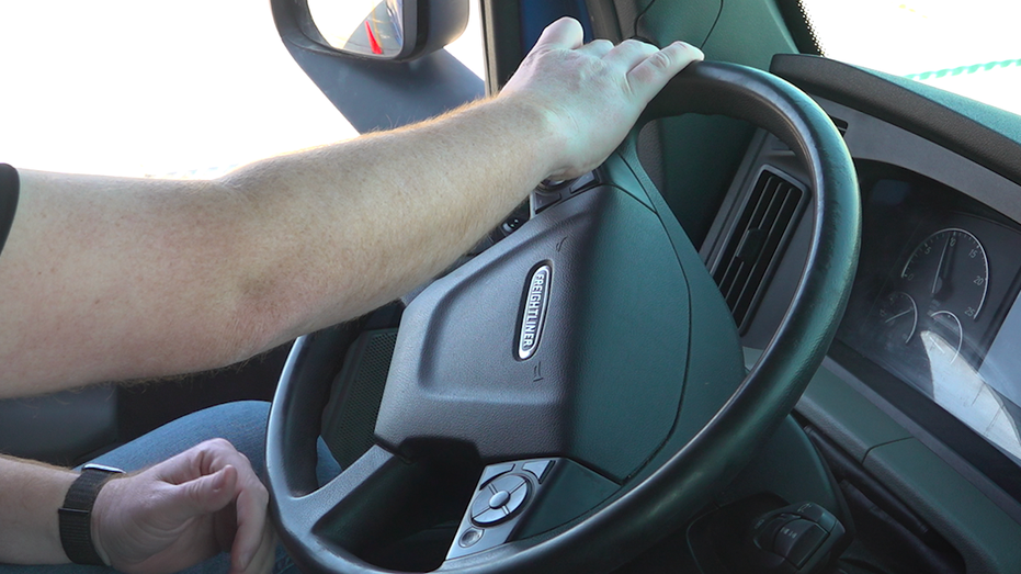 A truck driver with this hand on the wheel