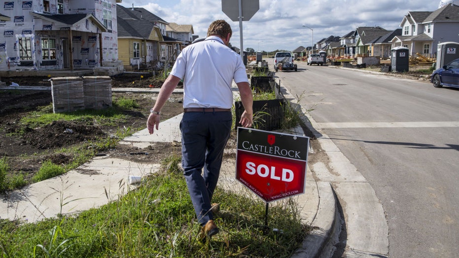 A housing manager moves a sold sign near a home.