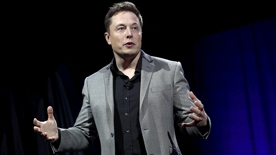 Elon Musk wearing a grey suit jacket as he speaks
