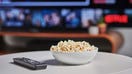 A bowl of popcorn and TV remote control on a coffee table, with Netflix streaming on a television in the background, taken on March 6, 2020. 