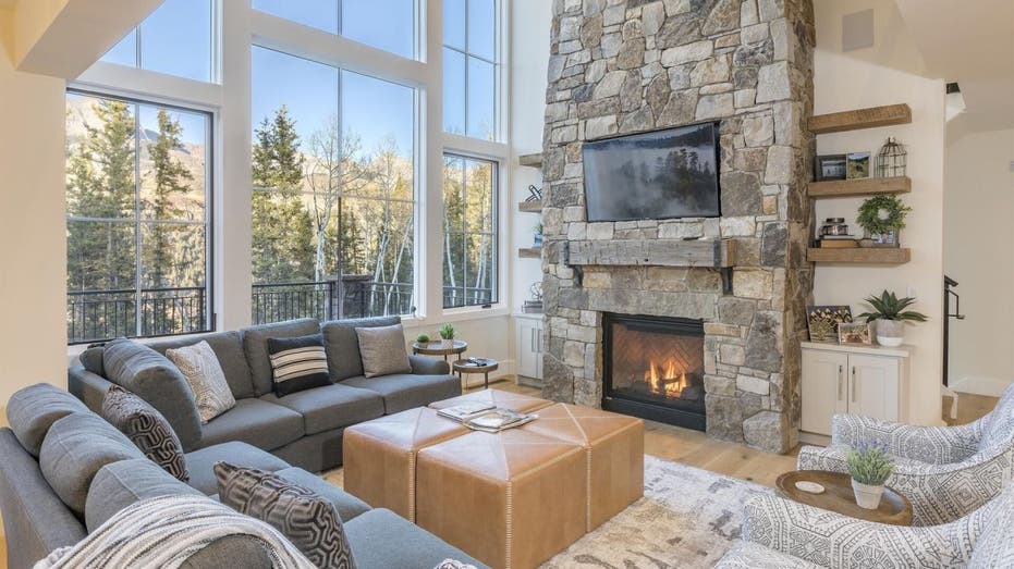 The Overlook Haus vacation home on Vrbo is located in Telluride, Colorado.  This interior photo shows that it has a stone fireplace, wooden shelves and large windows.