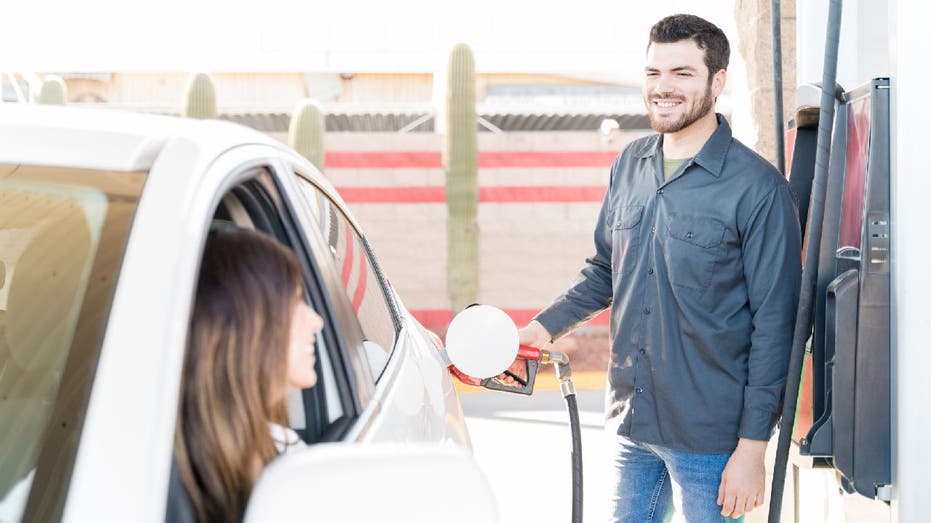 Gas station attendant pumps gas in white car and smiles while he works