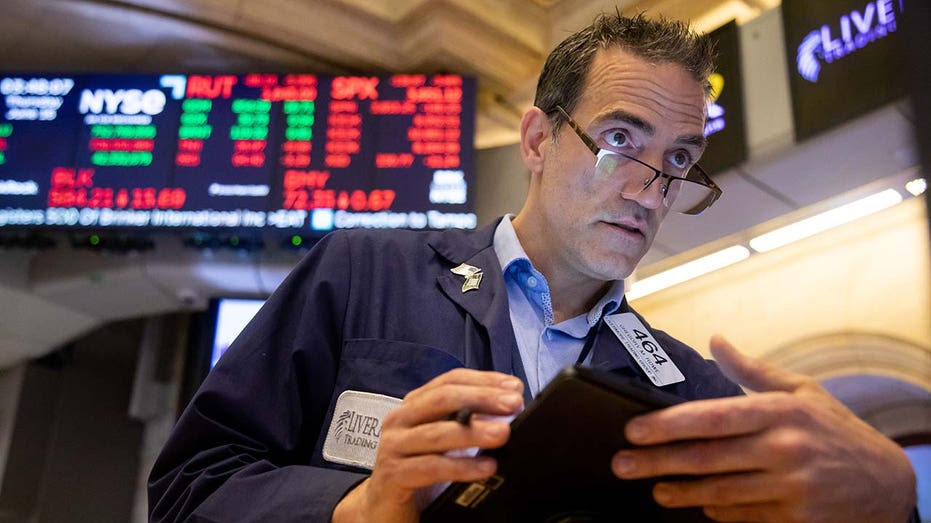 stock trader holds an iPad with the NYSE price board lit up behind him