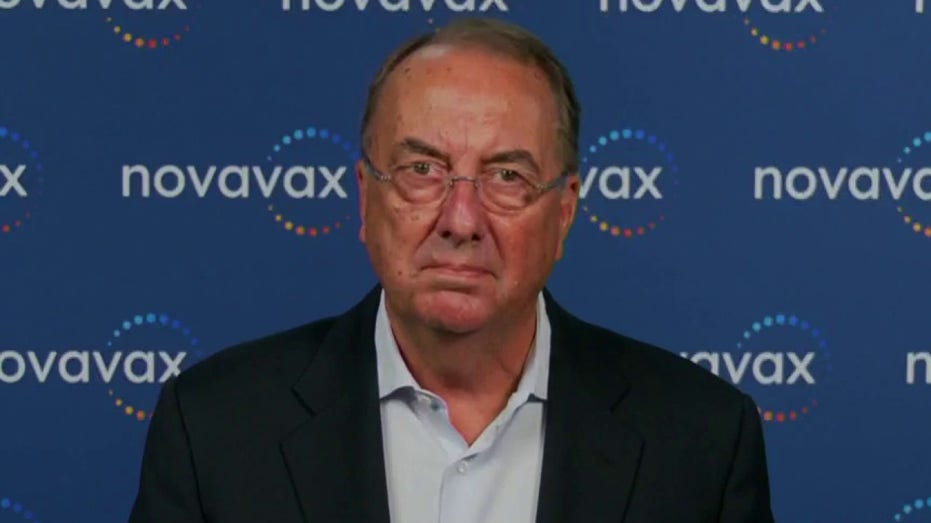 CEO Stanley Erick, wearing a dark blazer and shirt, speaks in front of a Novavax logo