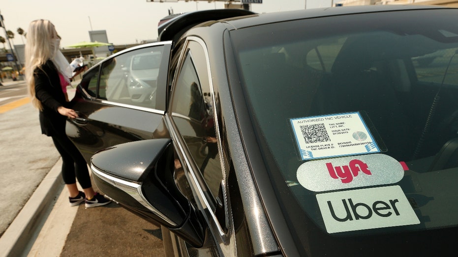 A woman enters a vehicle with Uber and Lyft stickers