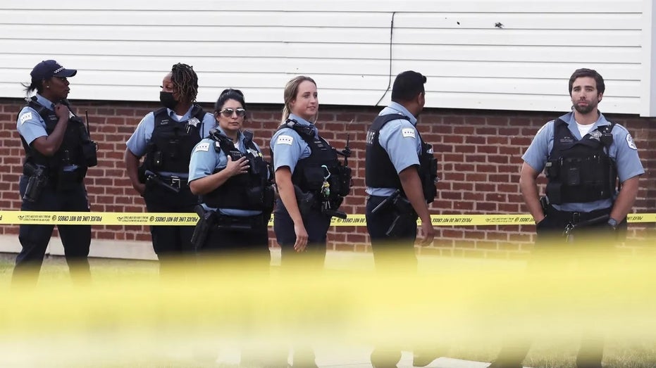 Several uniformed Chicago police officers standing behind yellow police tape