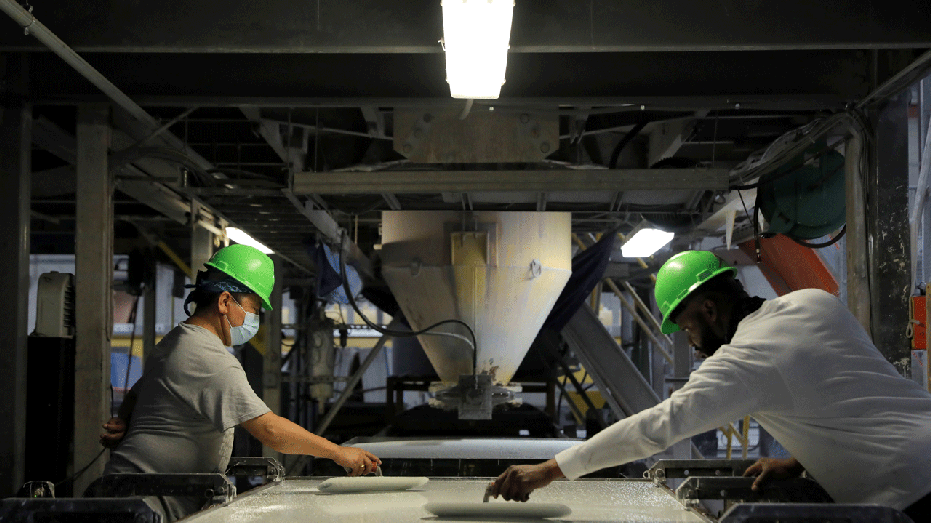 Two workers with green hard hats pour out a mixture in an IceStone factory