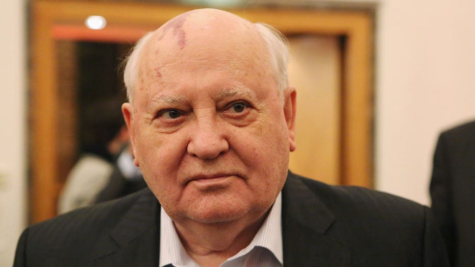 Gorbachev wears a dark suit with a white button down shirt