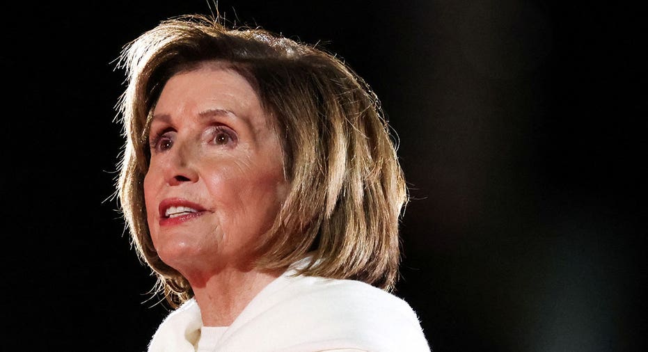 Nancy Pelosi in white suit looks out at crowd while on stage