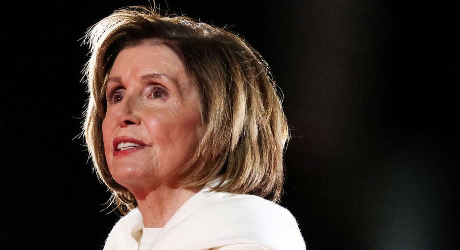 Nancy Pelosi in white suit looks out at crowd while on stage