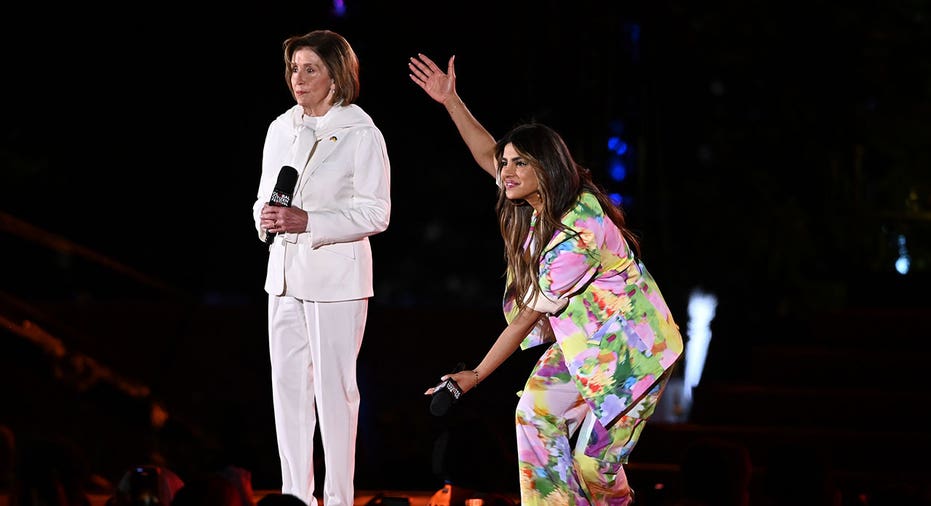 Nancy Pelosi (left) wears white pantsuit while Priyanka Chopra (right) holds up her arms showing off Pelosi