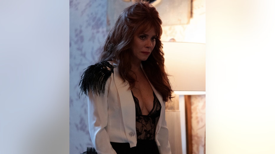 Anna Friel in a white jacket and black lace bodysuit.