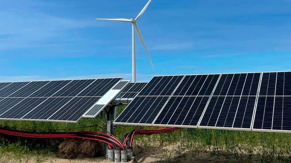 Wires connected to solar panels in front of wind turbines