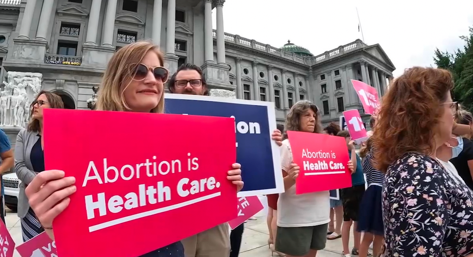 Protesters holding signs in front of the Pennsylvania State capitol. One sign reads 'Abortion is Health Care.' 