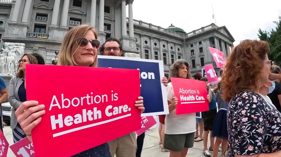 Protesters holding signs in front of the Pennsylvania State capitol. One sign reads 'Abortion is Health Care.'