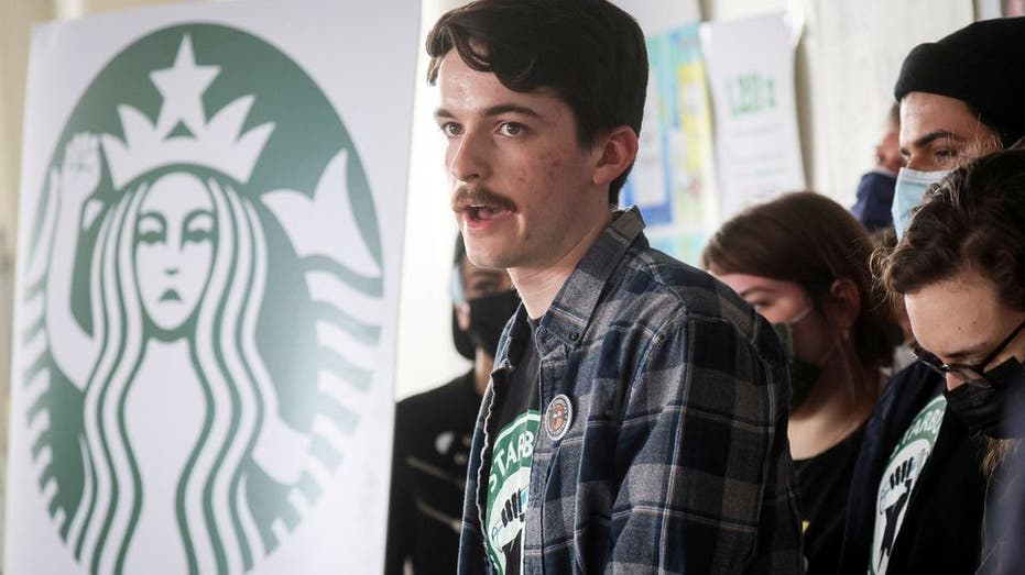 Starbucks worker with mustache with Starbucks logo banner in background