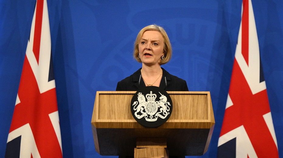 Liz Truss speaks at a wooden podium in front of a blue background