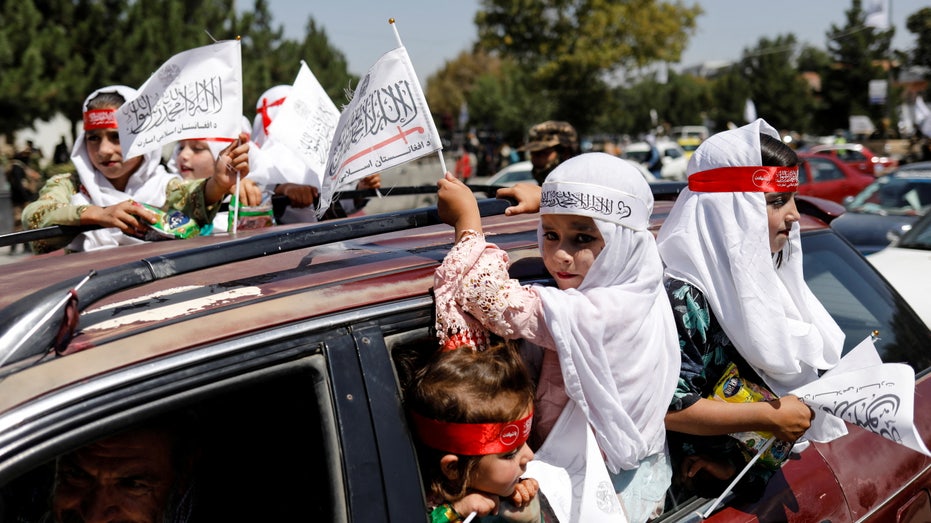 Des filles afghanes portent les drapeaux de l'Émirat islamique alors qu'elles participent au premier anniversaire du retrait des forces américaines d'Afghanistan