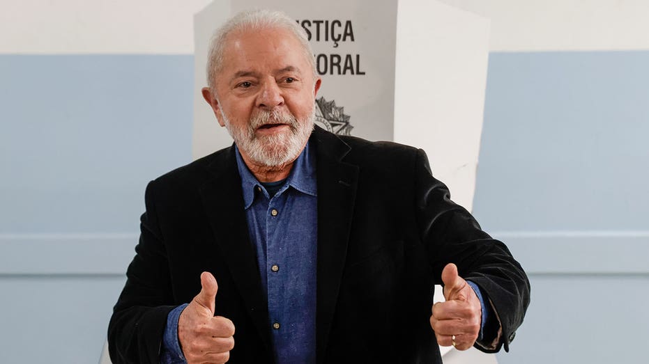 Lula puts two thumbs up while wearing a black blazer at an event 