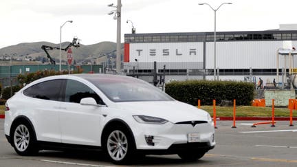 A Tesla vehicle drives past Tesla's factory in California. 