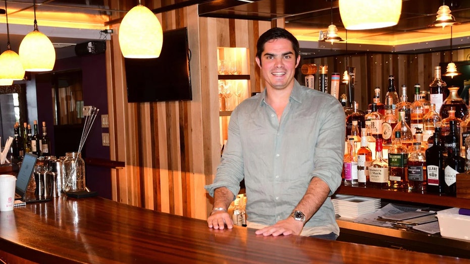 Man in green button-down shirt stands behind the bar