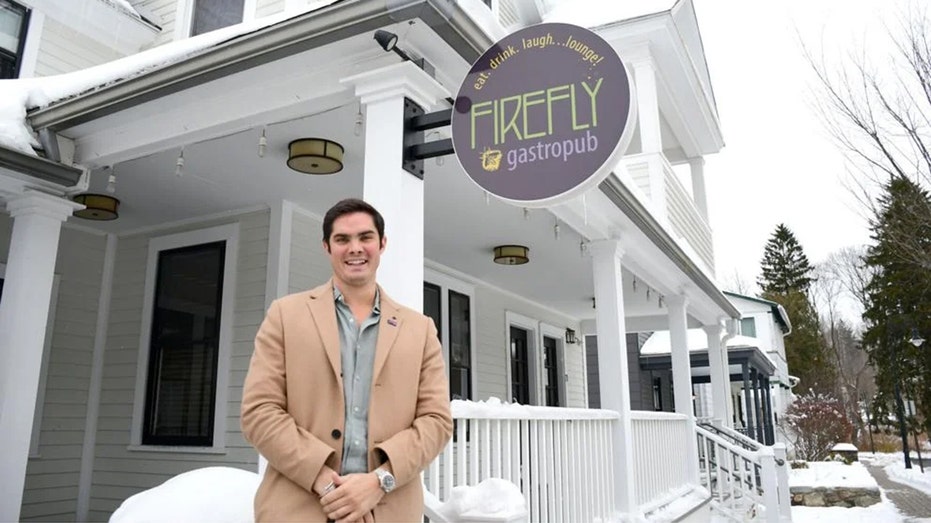 Man in camel coat with clasped hands wearing expensive watch outside restaurant
