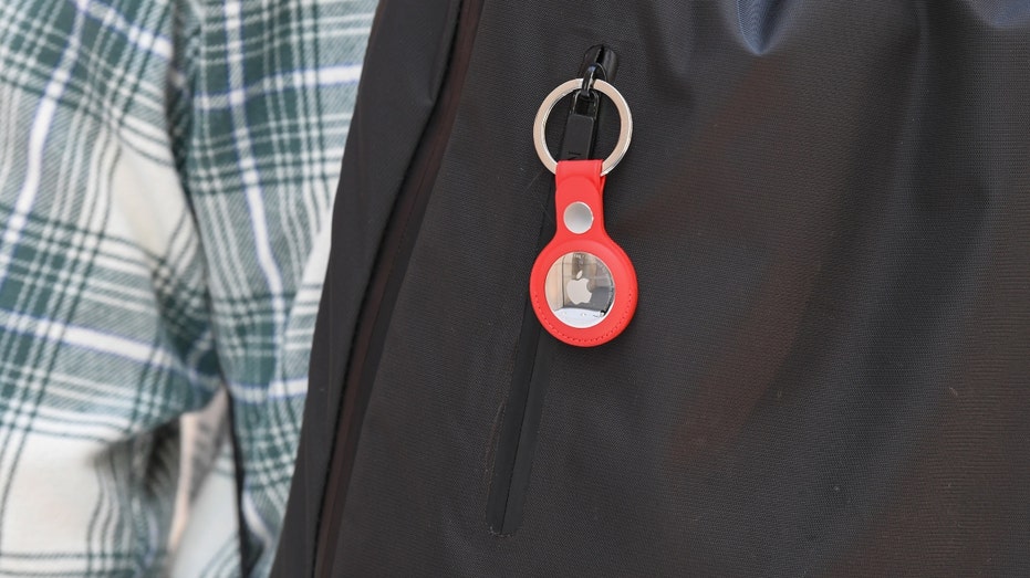 An Apple AirTag device hangs off a black backpack