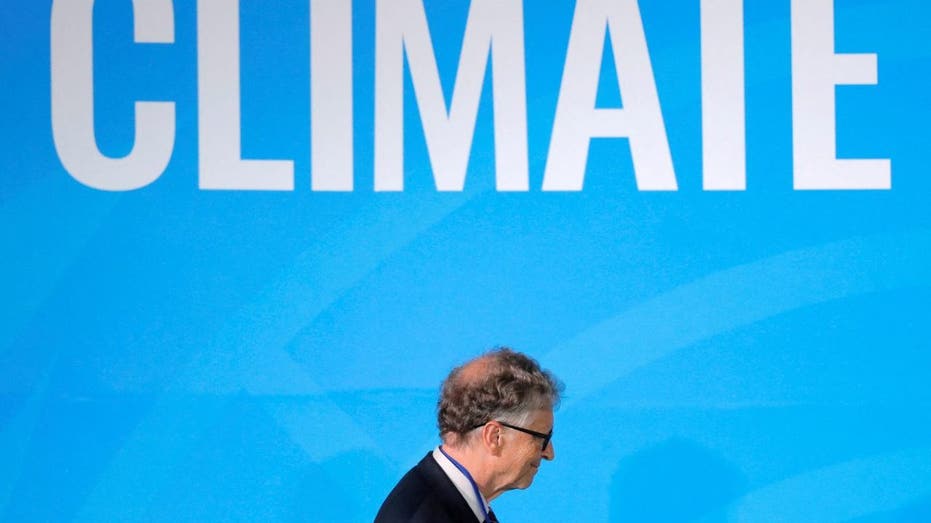 Bill Gates walks by a wall with the word "Climate" written on it.