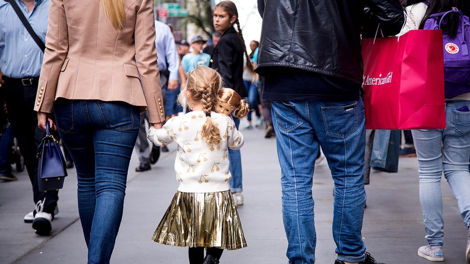 Child carries American Girl doll as parents carry bag