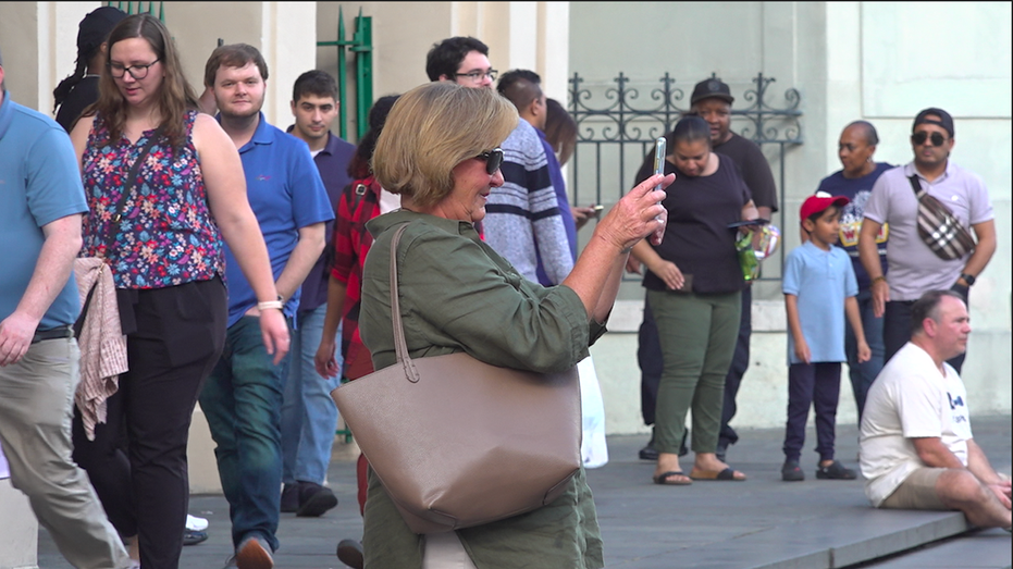 A woman holds up her phone to take a picture surrounded by other tourists in the French Quarter
