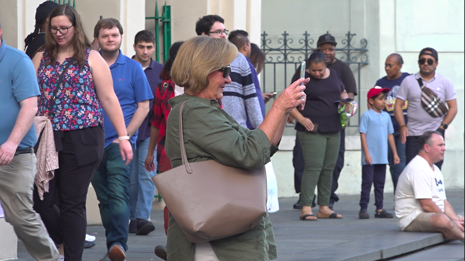 A woman holds up her phone to take a picture surrounded by other tourists in the French Quarter