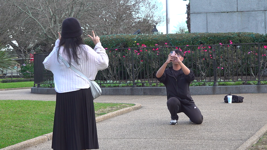 A man crouches down to take a photo of a woman who is posing with peace signs in New Orleans' French Quarter