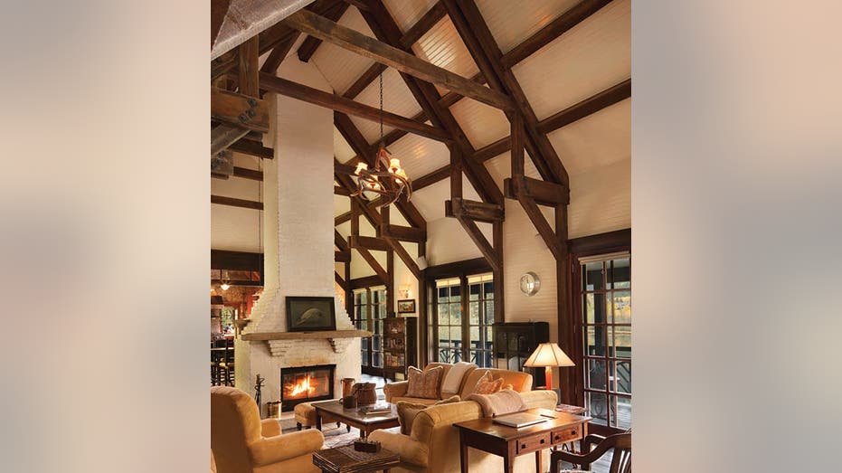 An illuminated fire burns in a great room with extremely tall ceilings, dark exposed beams, and many seating options