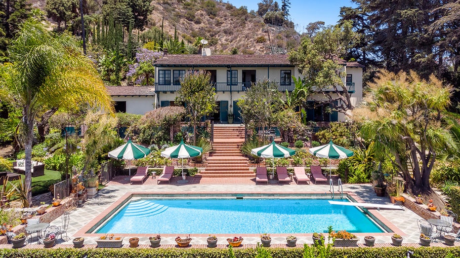 Backyard features a pool with several lounge chairs and green and white umbrellas 