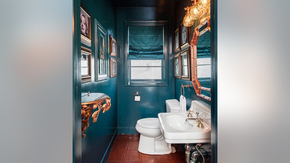 Teal powder bathroom with some copper accents and lots of artwork on the walls