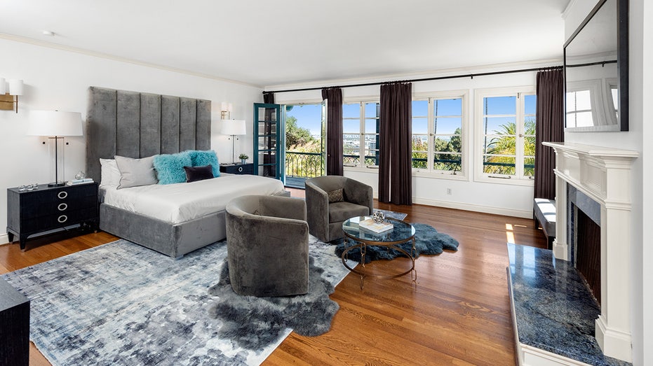 A grey bed with bright turquoise pillows and two dark grey swivel chairs in front of the bed