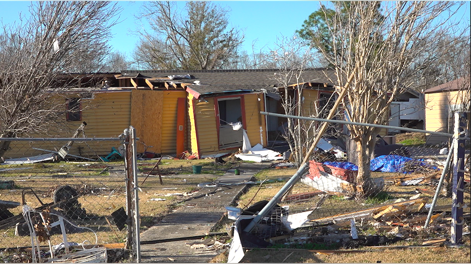 Damaged home with roof damage and debris in the front yard