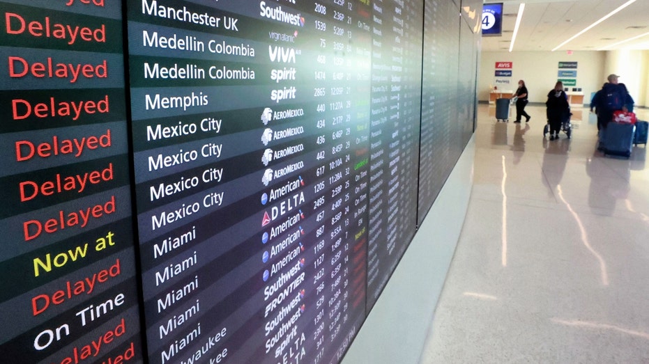 Passengers walk past a flight status board