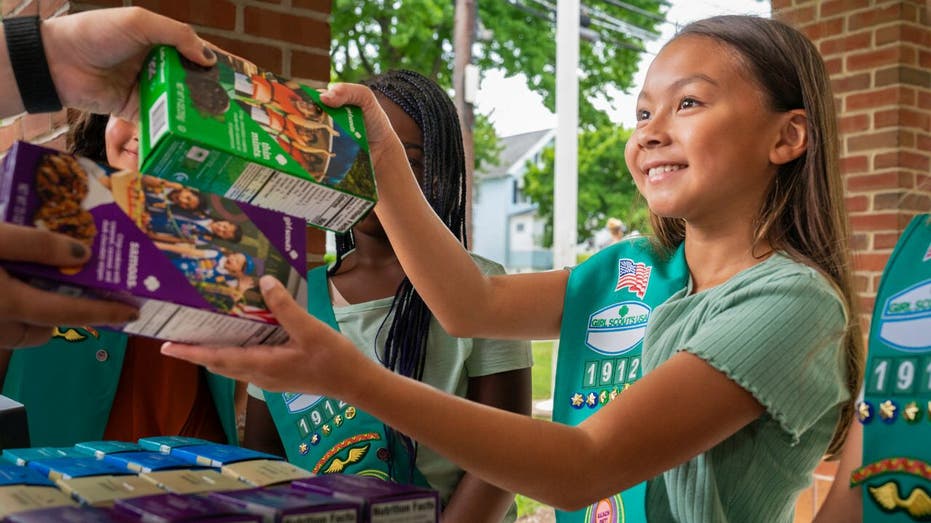 Girl Scout hands cookie boxes to adult